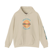A beige pullover hoodie with a colorful sunset graphic on the chest reading 'OKANAGAN LAKE LIFE' and teal text running down one sleeve, shown on a plain white background.
